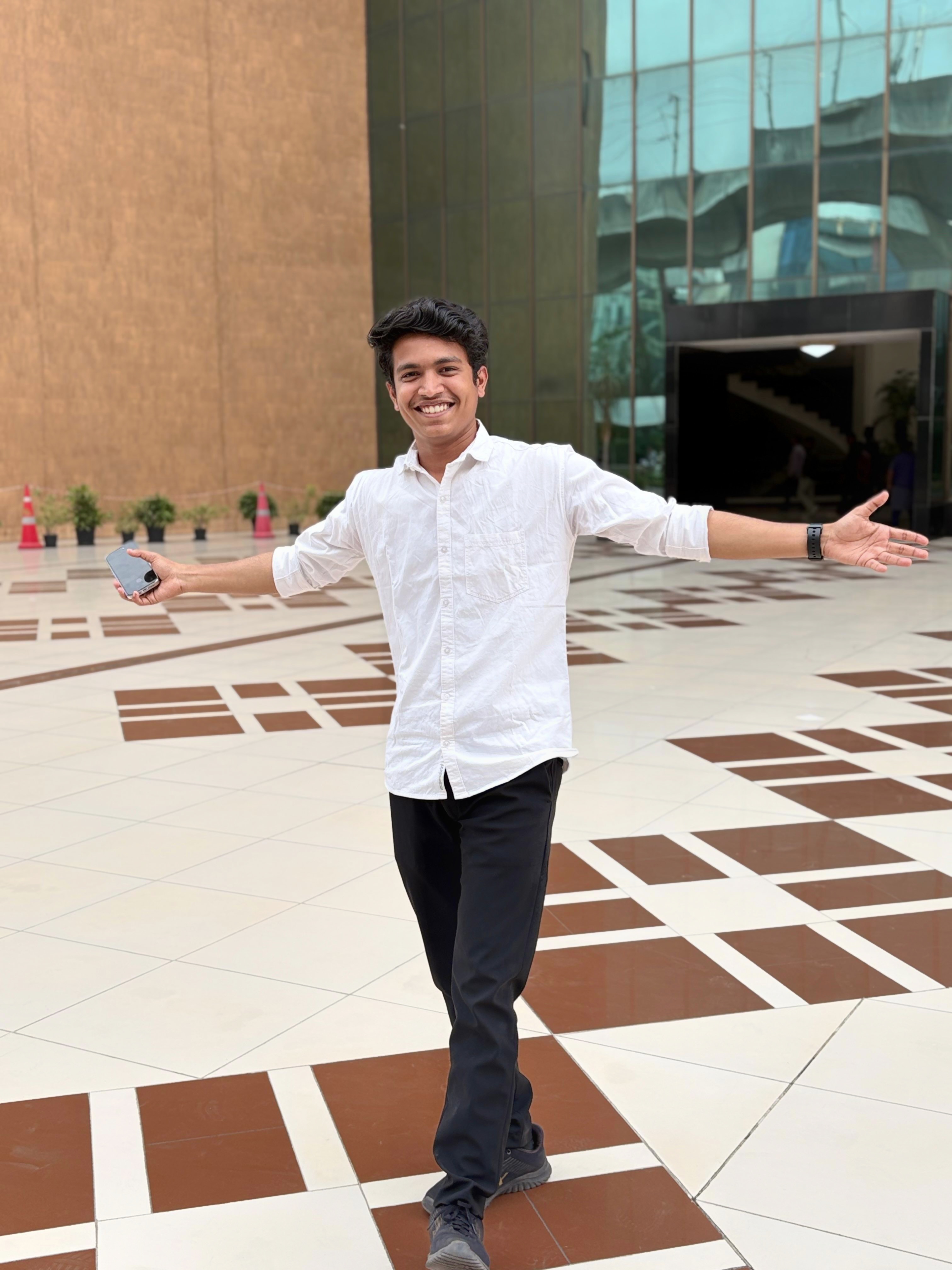 Prathamesh Kasar in a white shirt, arms open, outside an office building